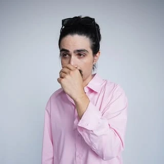 Johnny Maconny wearing a pink shirt against a light gray background.